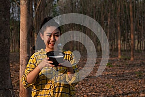 Portrait gardener young asea woman hand holding a full cup of raw para rubber milk of tree in plantation rubber tapping form