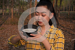 Portrait gardener young asea woman look at a full cup of raw para rubber milk of tree in plantation rubber tapping form Thailand,