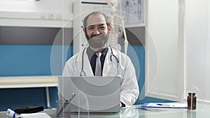 Portrait of general practitioner working on laptop at desk