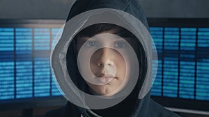 Portrait of a genius boy hacker prodigy in the hood on the background of monitors with program code. Young Wanted Hacker