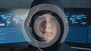 Portrait of a genius boy hacker prodigy in the hood on the background of monitors with program code. Young Wanted Hacker