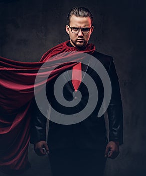 Portrait of a genius superhero in a black suit with a red tie on a dark background.