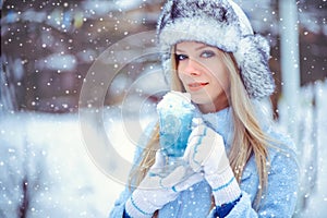 Portrait of a gentle glamorous woman in a winter hat with a winter drinkIn cold tones, snow falls, artistic toning. Concept of re