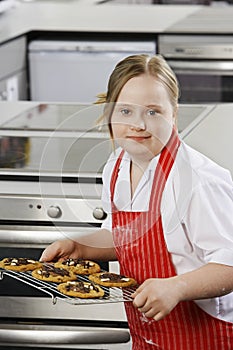 Portrait of girl (10-12) with Down syndrome carrying cookies on baking sheet