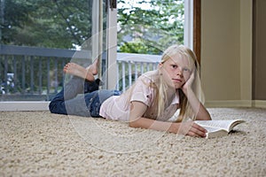 Portrait of girl 7-9 lying on carpet with book hand on chin