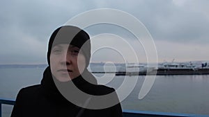 Portrait of a girl in a black dress on the pier in winter cloudy day