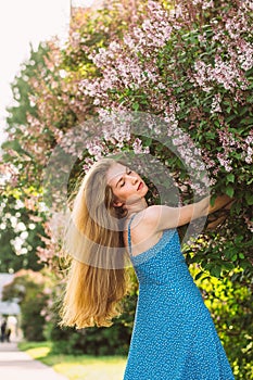 Portrait of girl with blond hair and closed eyes and blue dress among lilac