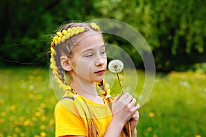 Portrait of a girl blowing on a dandelion flower in the open air. A child is having fun in the spring park. Blurred green