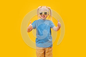 Portrait of girl in blue T-shirt and sunglasses showing thumbs up or like gesture with two hands. Copy space, mock up