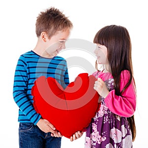 Portrait of girl and boy holding a big red heart shaped pillow