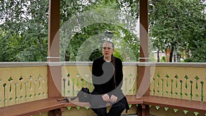 Portrait of a girl with braid dressed in black sitting in the gazebo in summer