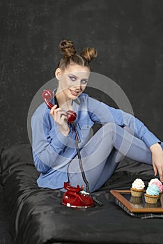 Portrait of girl with bright makeup and bun hairstyle in studio on black background. Woman holds retro phone and maffins