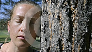 Portrait of a girl with closed eyes, leaning her head against a tree