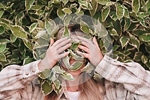 Portrait of a girl covering her face with green leaves.