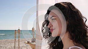 Portrait girl with curls, women smiles and drinks cocktail from oconut, wind develops female hair, summer season,