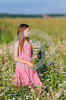 Portrait of girl in dress and straw hat on a chamomile field in summer