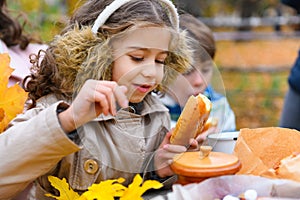 Portrait of a girl eating a bun. Happy family resting in autumn city park. People are sitting at the table, eating and talking.