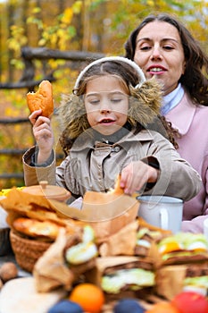 Portrait of a girl eating a bun. Happy family resting in autumn city park. People are sitting at the table, eating and talking.
