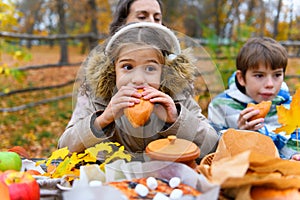 Portrait of a girl eating a bun. Happy family resting in autumn city park. People are sitting at the table, eating and talking.