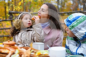 Portrait of a girl eating a bun. Happy family resting in autumn city park. People are sitting at the table, eating and talking.