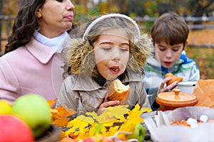 Portrait of a girl eating a bun. Happy family resting in autumn city park. People are sitting at the table, eating and talking.