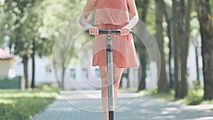 Portrait of a girl on an electric scooter riding in a park in the summer.