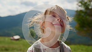 Portrait girl enjoying sunlight in mountains. Child putting face under sunshine.