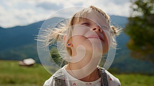 Portrait girl enjoying sunlight in mountains. Child putting face under sunshine.