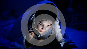 Portrait of beautiful girl with flashlight reading book in bed