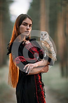 Portrait of girl in forest with owl in hand. Close-up.