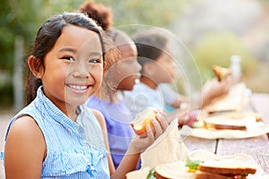 Portrait Of Girl With Friends Eating Healthy Picnic At Outdoor Table In Countryside