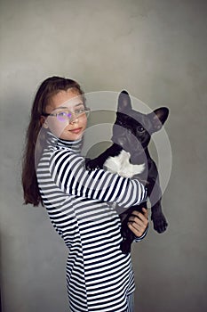 portrait of a girl with glasses holding a French bulldog dog in her arms . serious Caucasian teenage girl in a striped