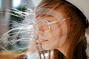 Portrait of a girl with glasses in a white dress and a white hat during a strong wind in a Park in Ufa