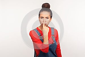 Portrait of girl with hair bun in overalls pointing nose doing lie gesture, suspecting trickster in falsehood, disbelief