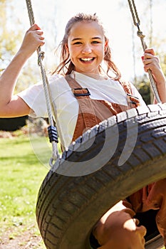 Portrait Of Girl Having Fun On Tyre Swing In Garden At Home