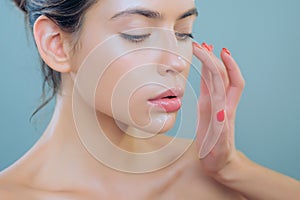 Portrait of girl with healthy clean skin. Woman putting anti-aging cream on face. Female model with natural nude makeup.