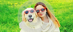 Portrait girl with her Golden Retriever dog wearing a sunglasses on green grass