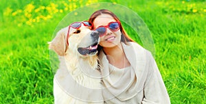Portrait girl with her Golden Retriever dog wearing a sunglasses on green grass