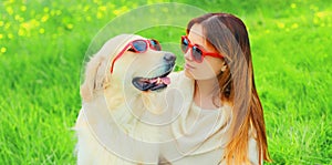 Portrait girl with her Golden Retriever dog wearing a sunglasses on green grass