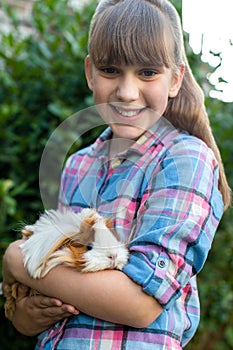 Portrait Of Girl Holding Pet Guinea Pig Outdoors In Garden