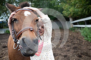 girl hugging pony horse muzzle at ranch