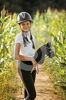 Portrait of a girl - a jockey in a helmet and a white T-shirt, who sits on a black toy horse in a corn field photo