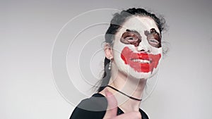 Portrait of girl with joker make up dances then smiles and shows humb up. White background