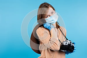 Portrait of a girl journalist with a camera in a summer hat, protective gloves and a medical mask looks at the camera. Tourism and