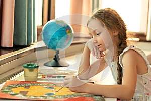 Portrait of girl kid is painting with colors gouache and brush picture while sitting at table on home room background.