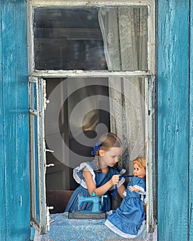 Portrait of girl kid tailor sew making doll& x27;s clothes on a children& x27;s sewing machine in the window of an old