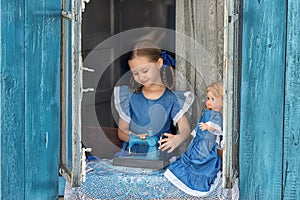 Portrait of girl kid tailor sew making doll& x27;s clothes on a children& x27;s sewing machine in the window of an old