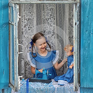 Portrait of girl kid tailor sew making doll& x27;s clothes on a children& x27;s sewing machine in the window of an old