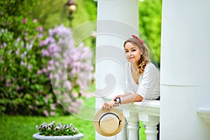 Portrait of a girl in a lilac blooming garden in spring in a white gazebo looking at the camera