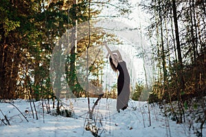 Portrait of a girl in a long dress, which stands in the winter Sunny forest among the trees. The girl stands in the pose of a tree